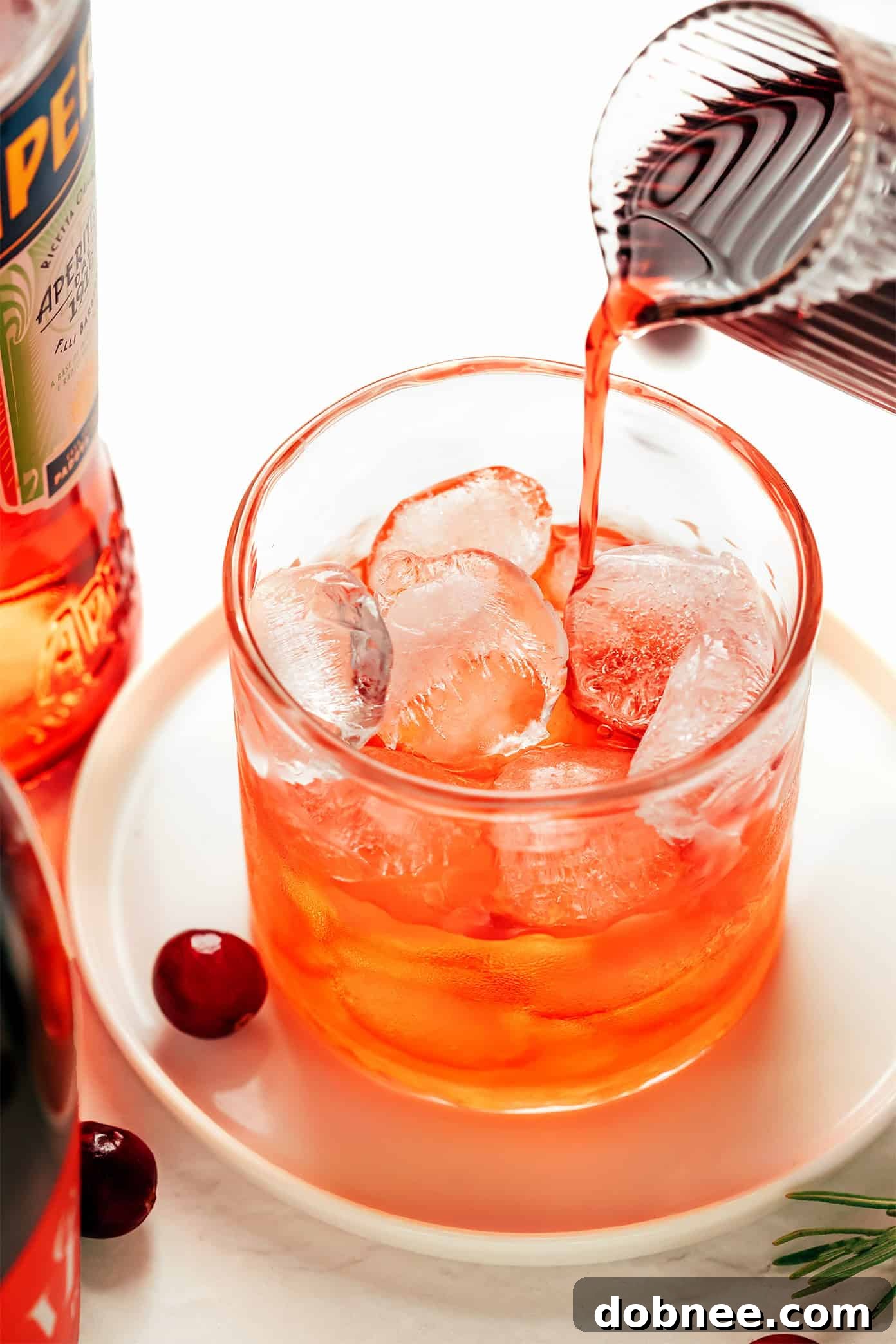 Hands holding a freshly made Cranberry Aperol Spritz with festive garnishes.