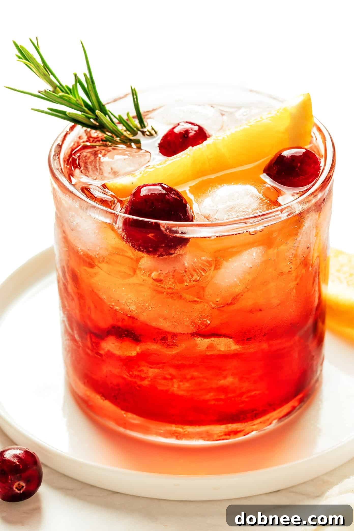A festive Cranberry Aperol Spritz, garnished with cranberries, orange, and rosemary, set against a cozy holiday backdrop.