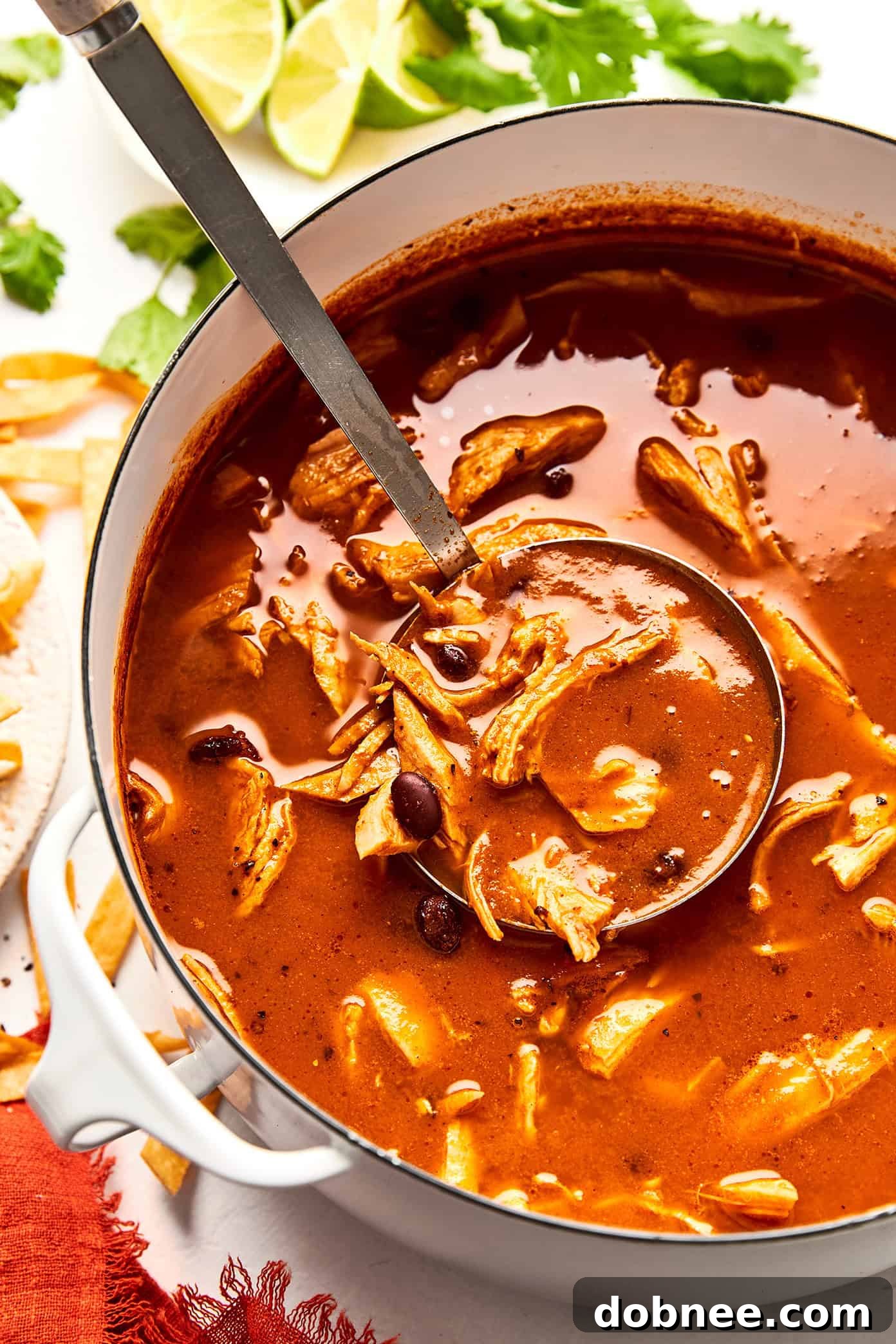 A wide shot of a delicious turkey tortilla soup being served into bowls, with various toppings on the side.
