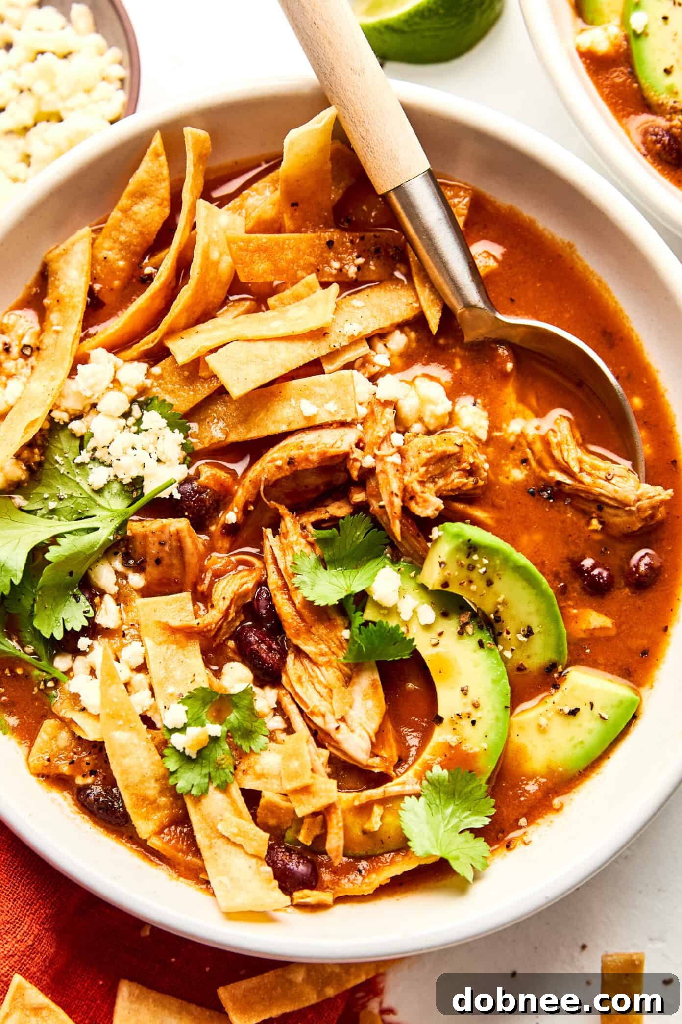Overhead shot of Turkey Tortilla Soup in bowls, with a variety of fresh toppings including avocado, cilantro, and lime wedges.