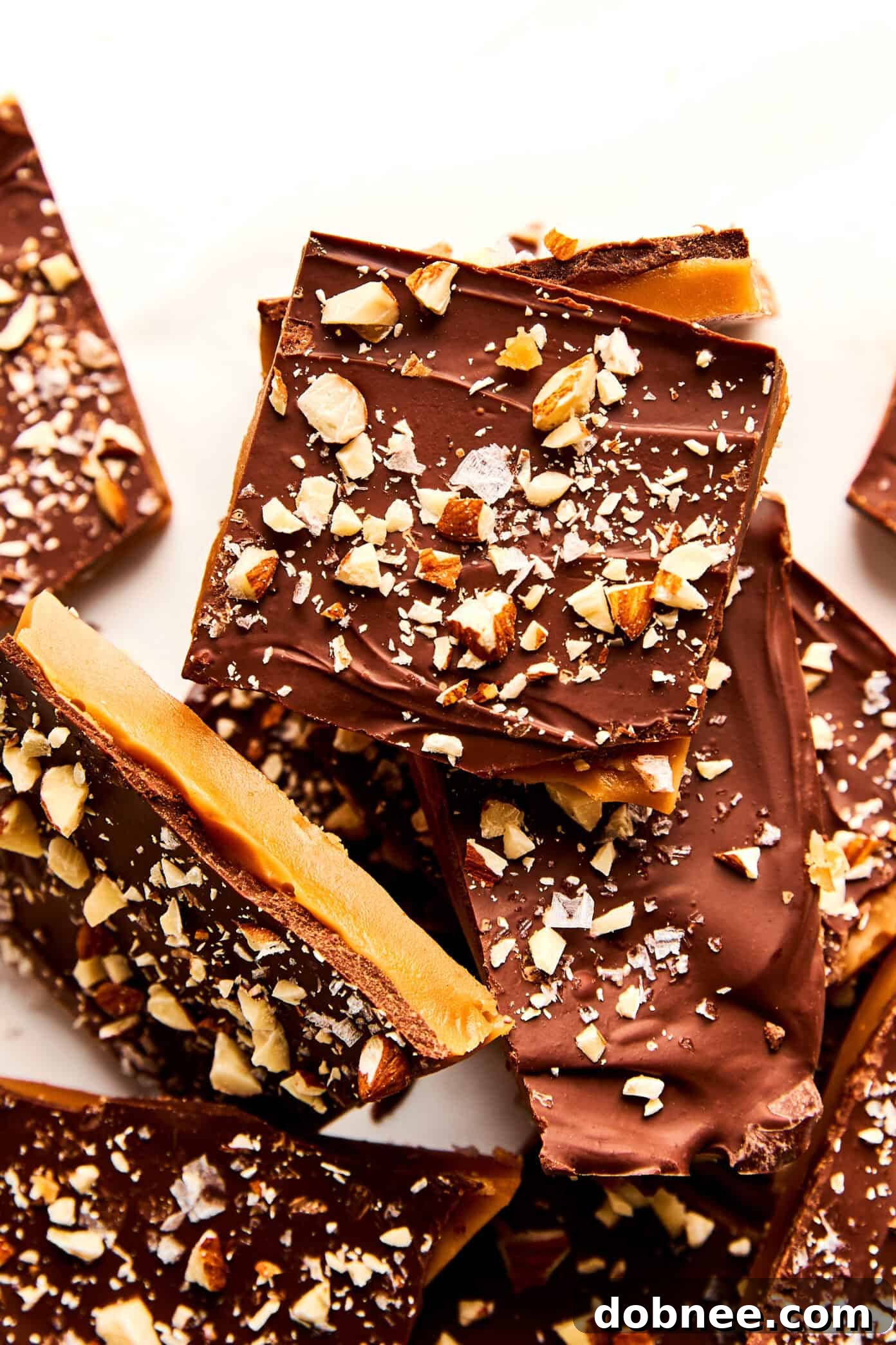 Close-up of a hand breaking a piece of homemade toffee, showing its crisp texture.
