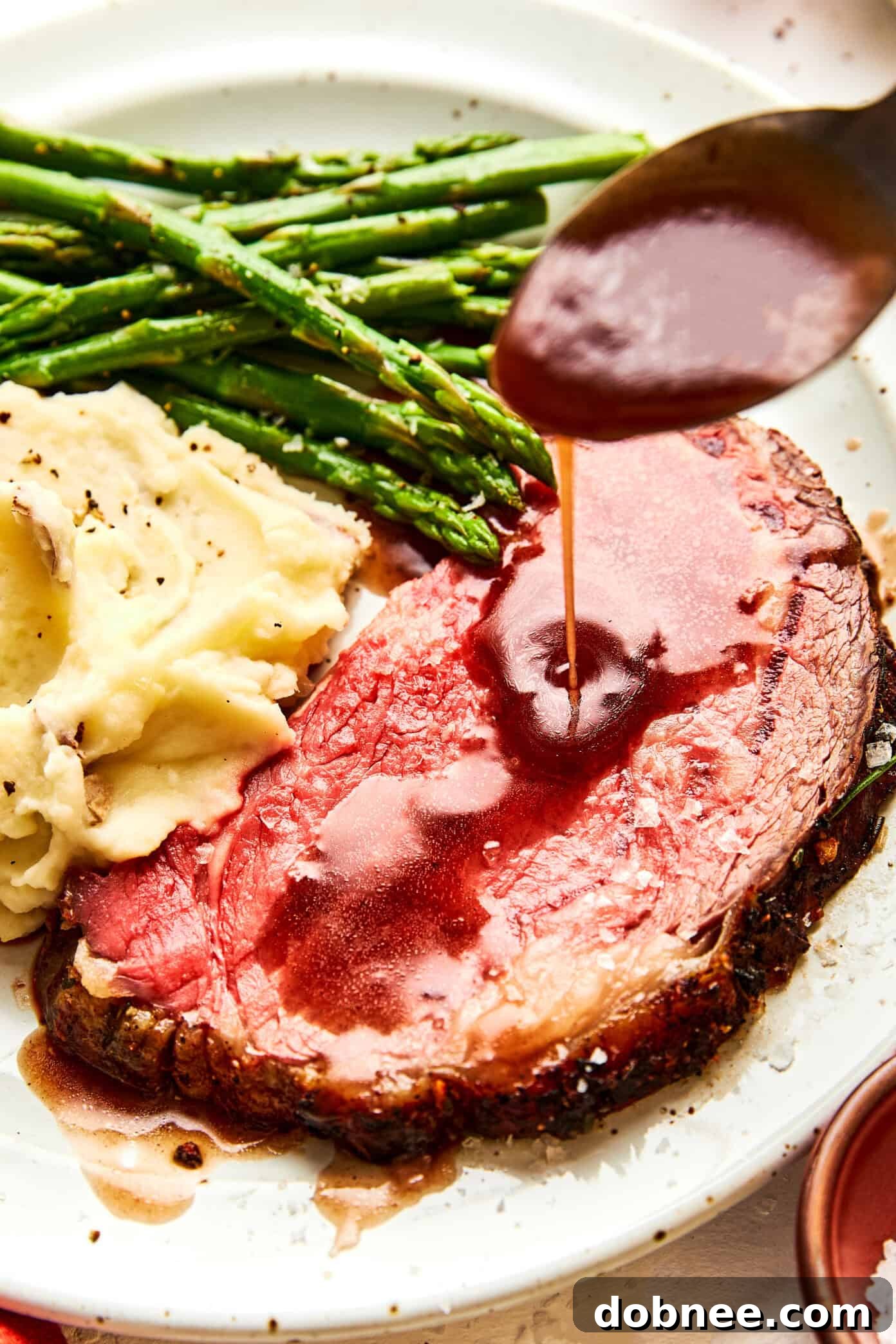 A succulent slice of prime rib, artfully arranged on a plate, drizzled with glistening au jus and sprinkled with flaky sea salt.