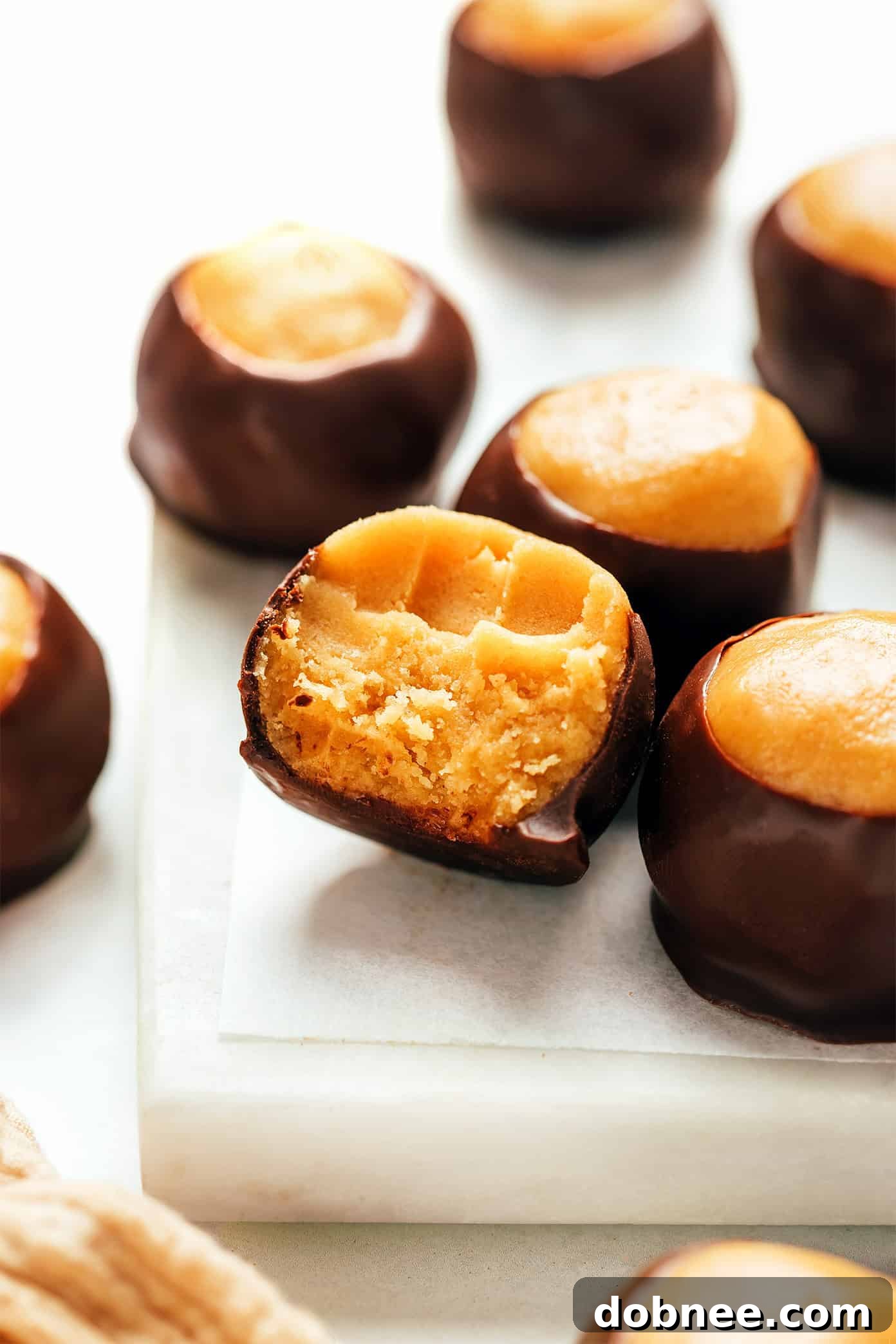A buckeye with a bite taken out, revealing the smooth peanut butter center and dark chocolate coating.