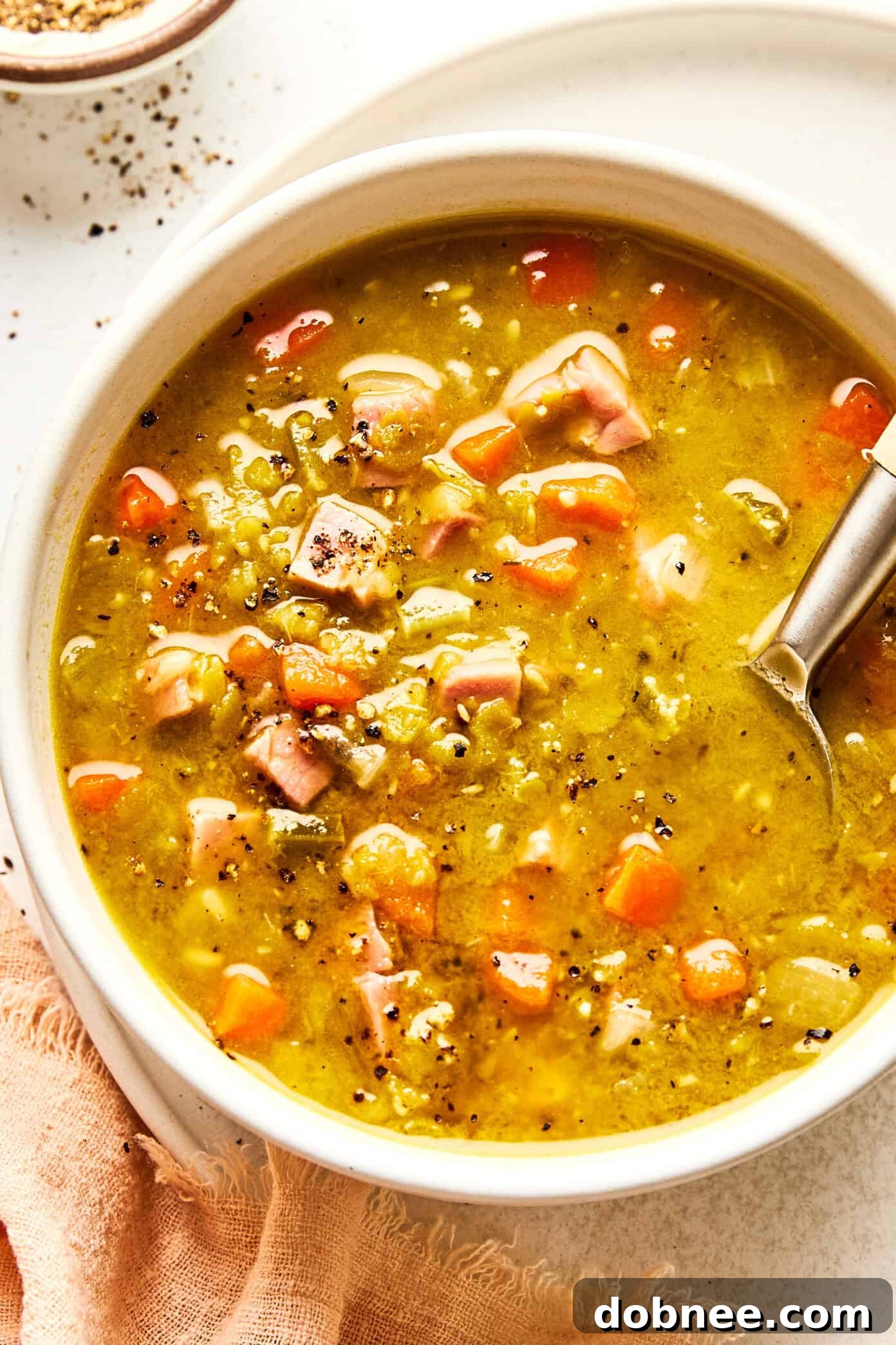 A steaming bowl of homemade split pea soup with ham, garnished with fresh parsley.