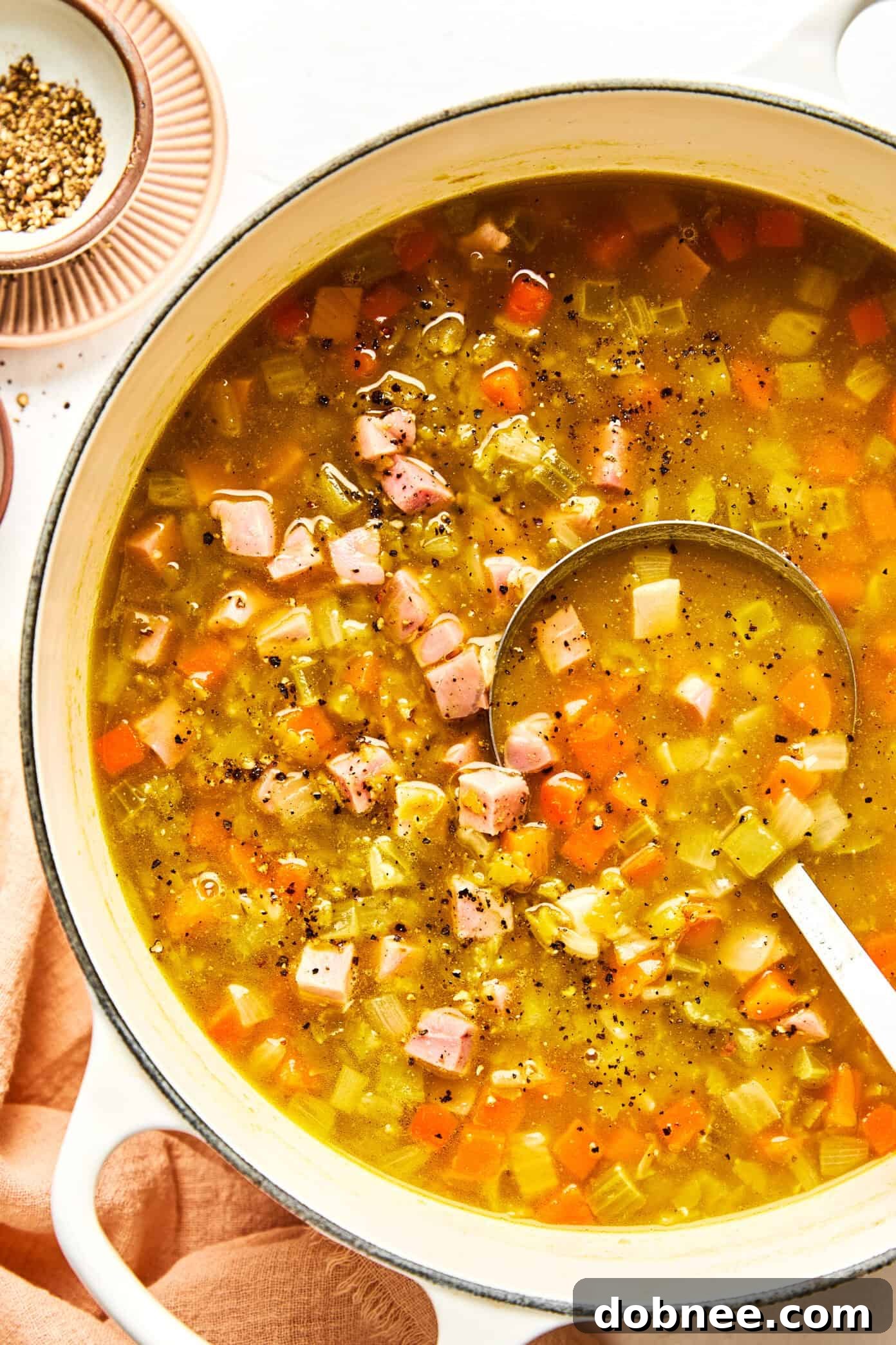 A ladle serving split pea soup with ham into a bowl.