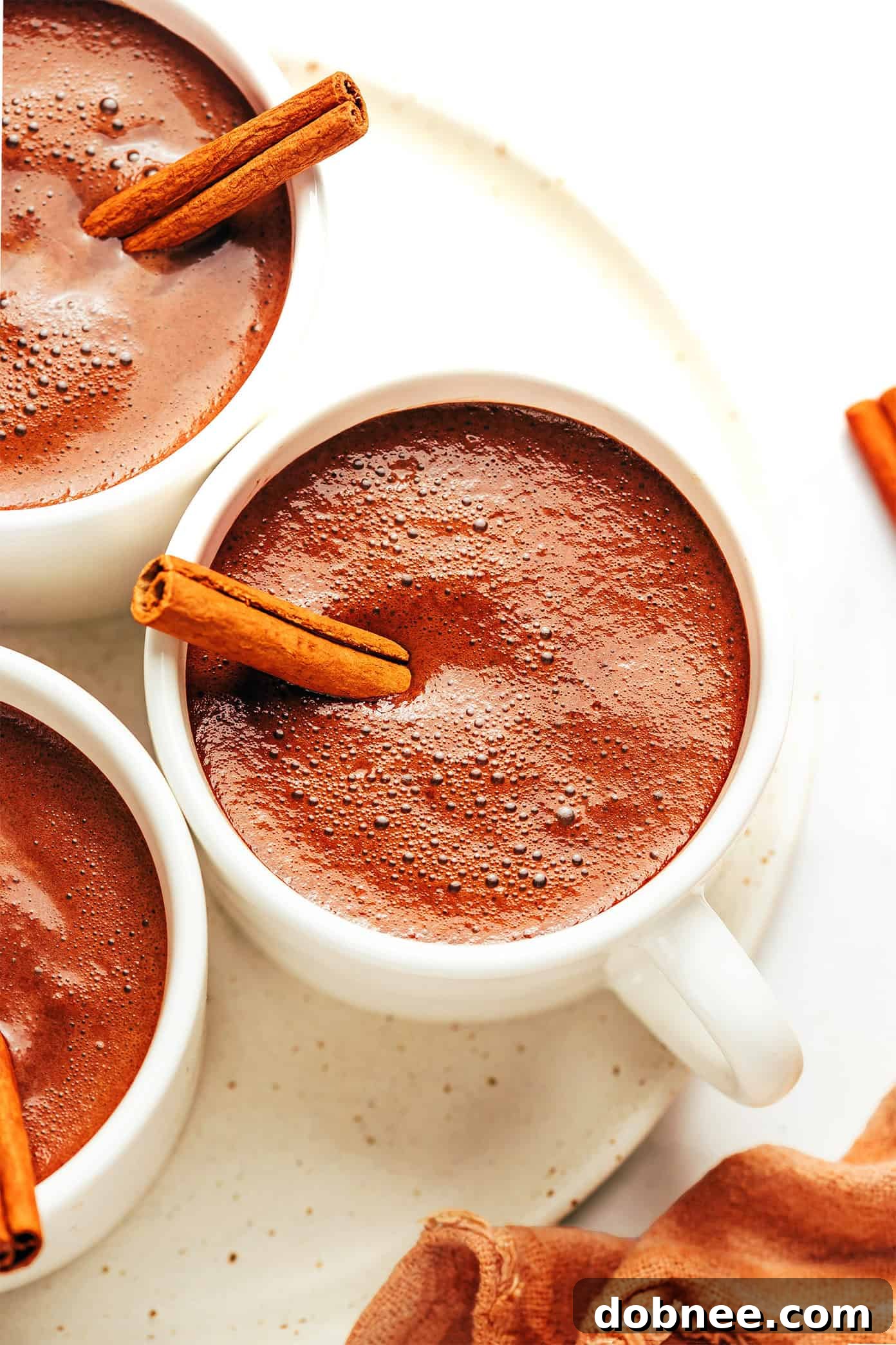 A steaming mug of authentic Mexican Hot Chocolate, beautifully garnished with a cinnamon stick and a sprinkle of spices, set on a rustic wooden table.
