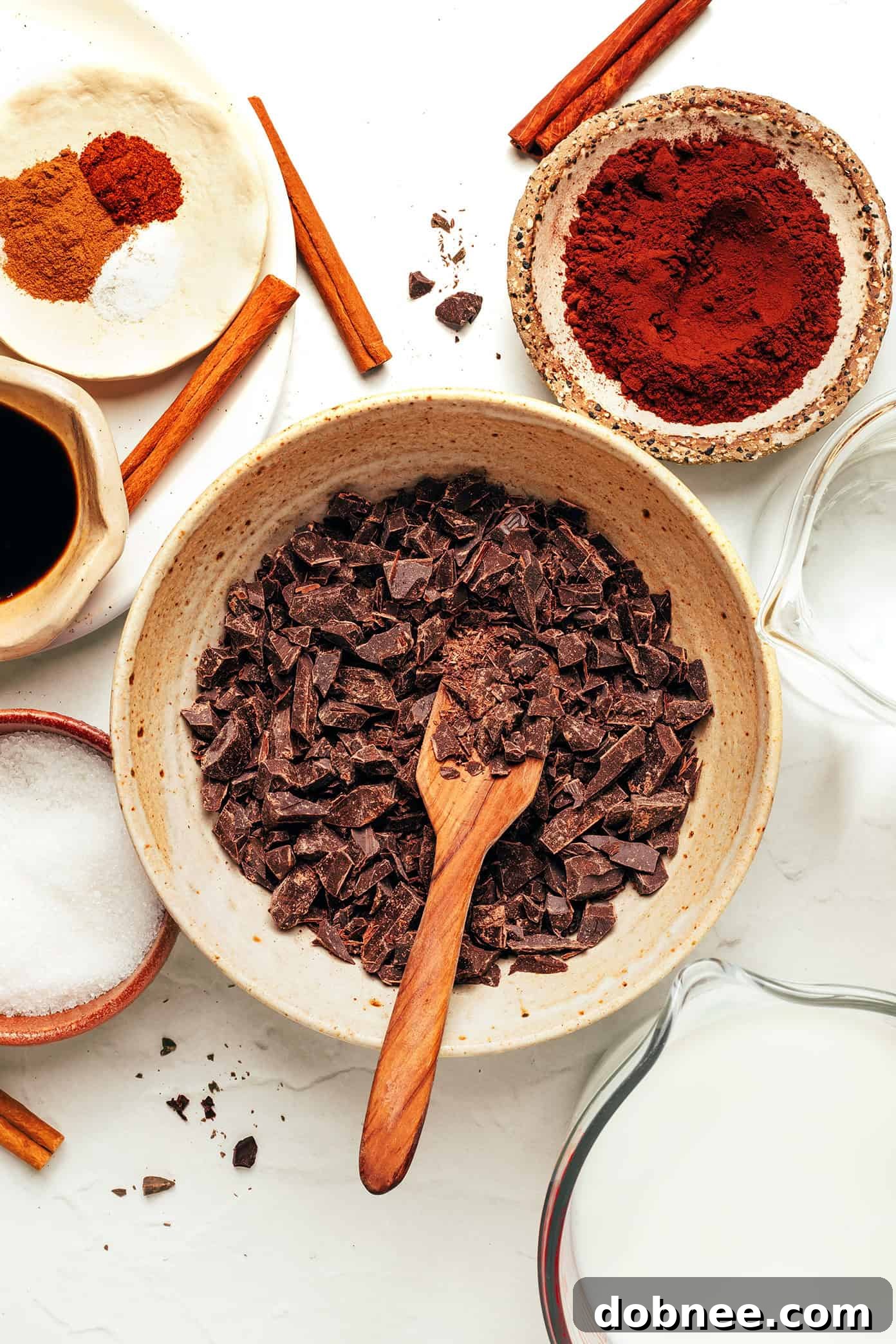 A selection of high-quality ingredients for Mexican Hot Chocolate, including dark chocolate bars, cinnamon sticks, whole chilies, and a measuring spoon, beautifully arranged.