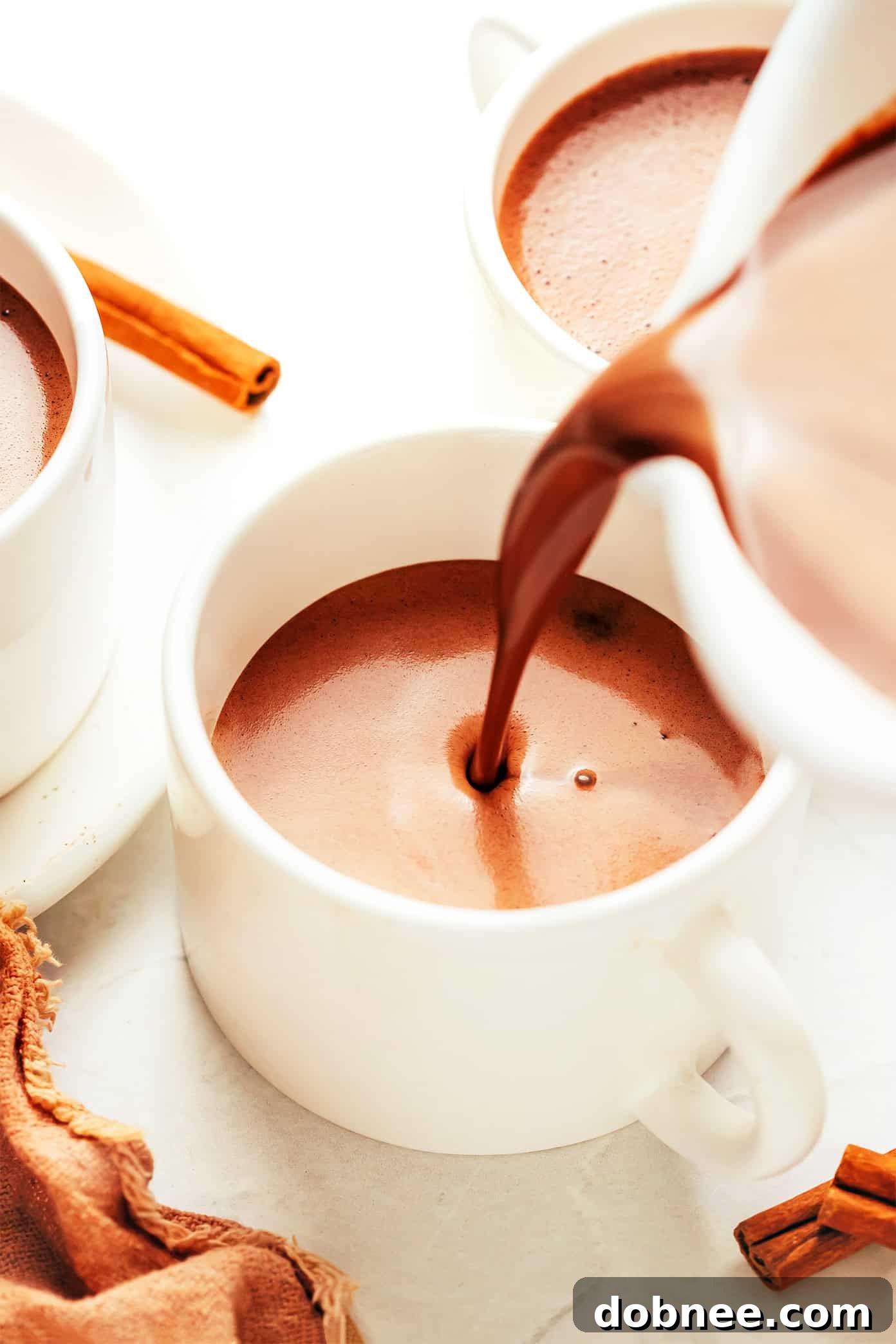 Two mugs of Mexican Hot Chocolate, one topped with fluffy whipped cream and the other with a fragrant cinnamon stick, invitingly placed on a wooden backdrop.