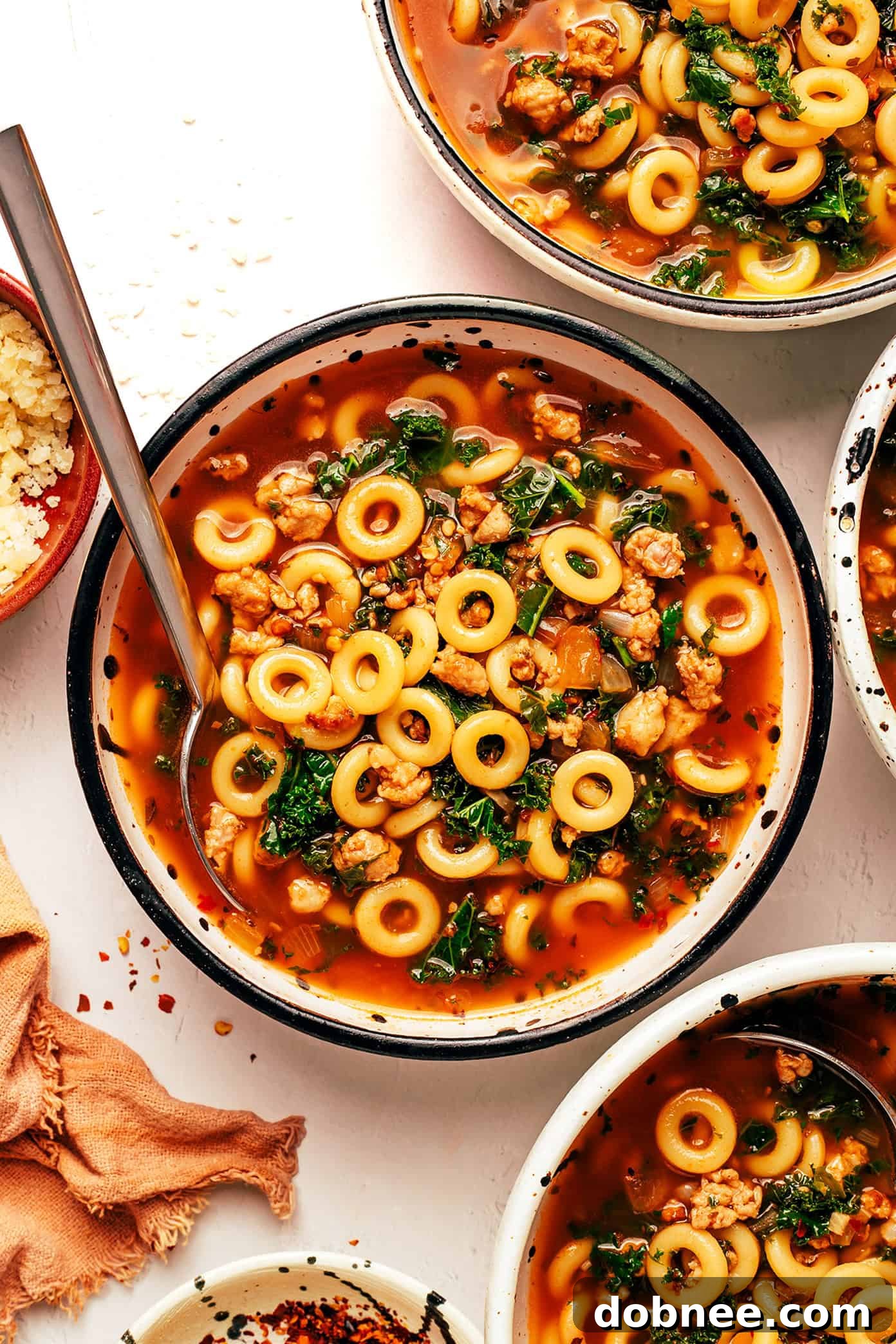 A steaming bowl of Spaghettios and Sausage Soup, ready to be served, with a sprinkle of Parmesan.