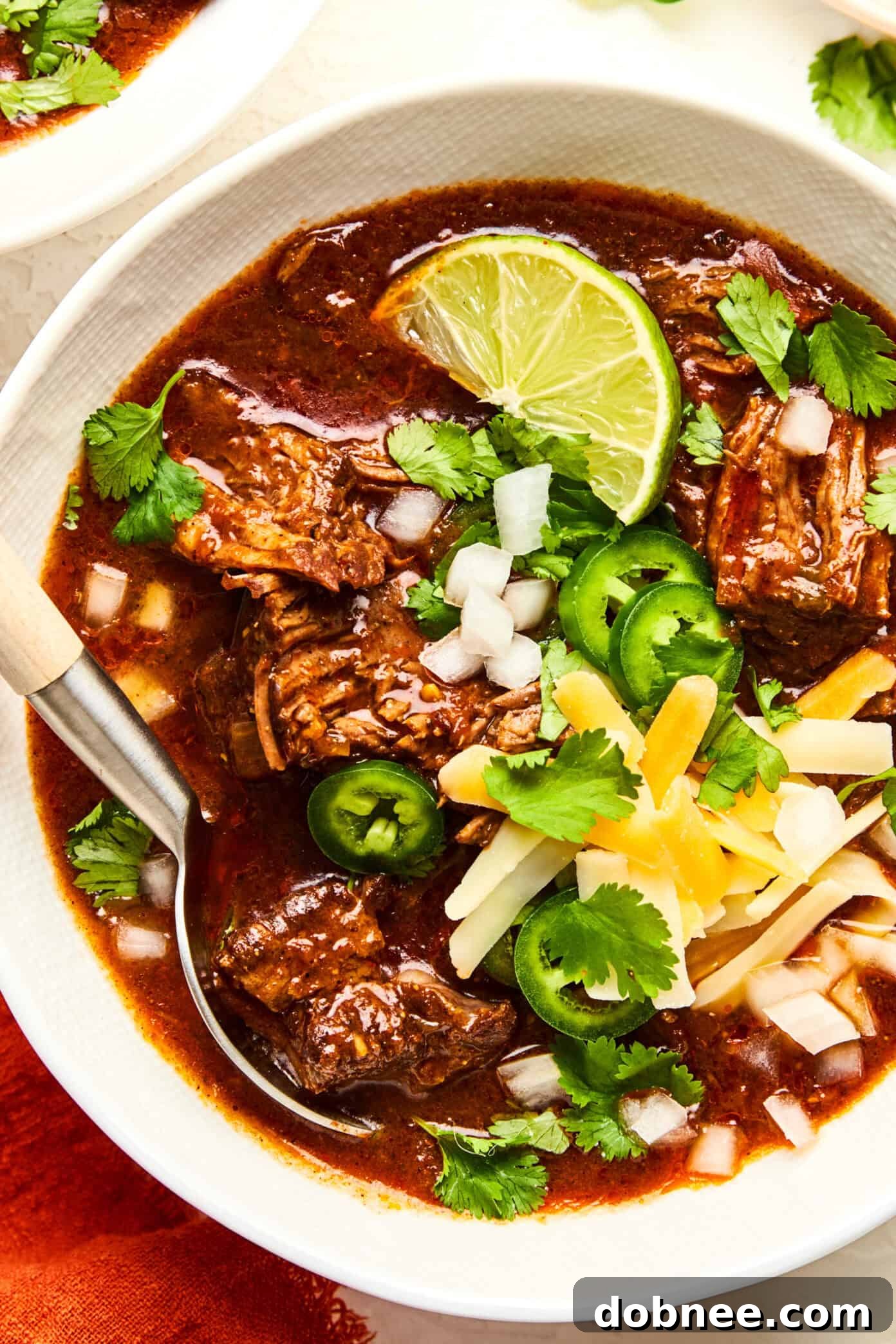 A serving of Texas Chili topped with grated cheese, diced onions, and cilantro.