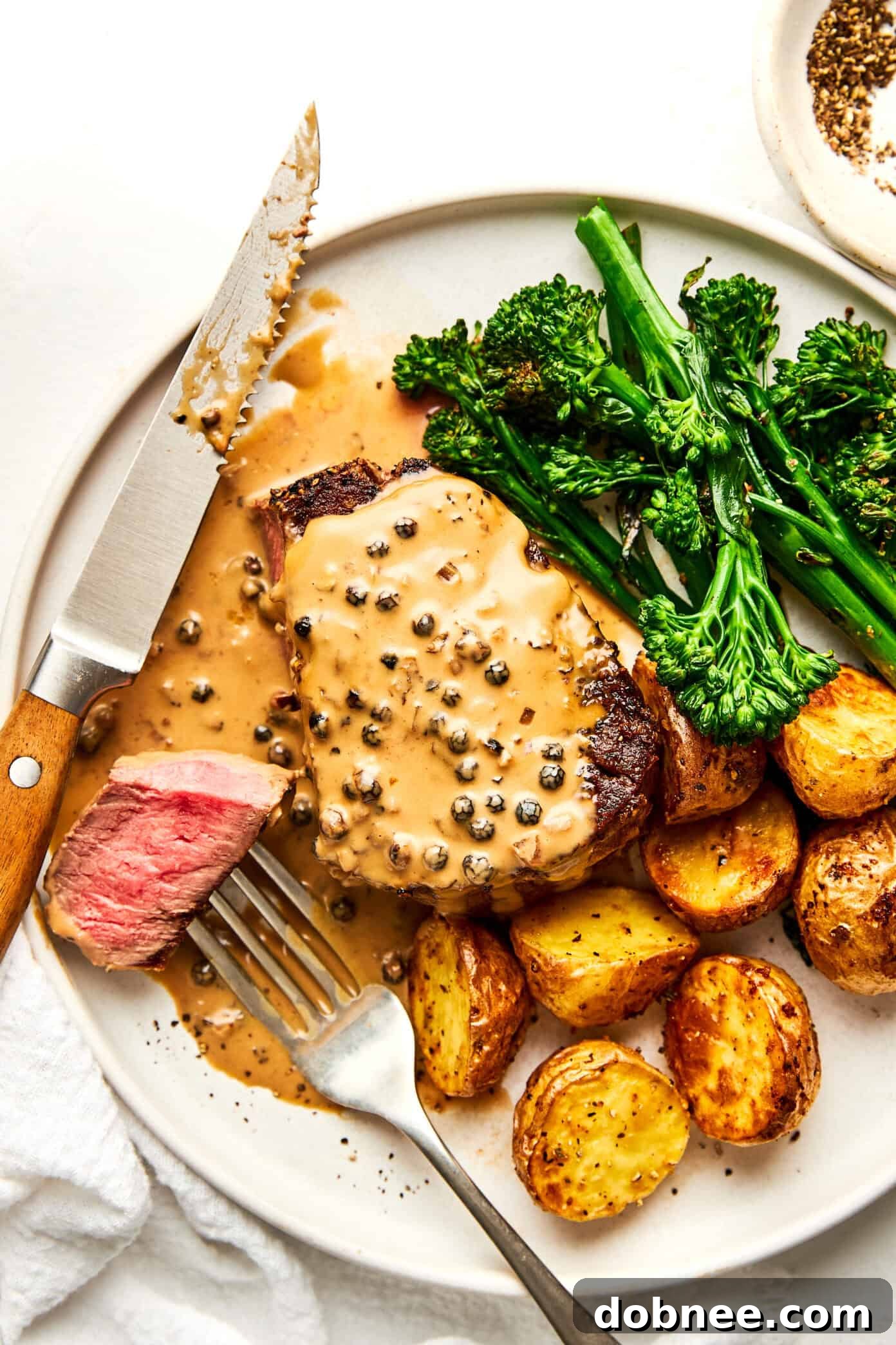 Seared Filet Mignon with Peppercorn Sauce on a plate, garnished with fresh herbs.