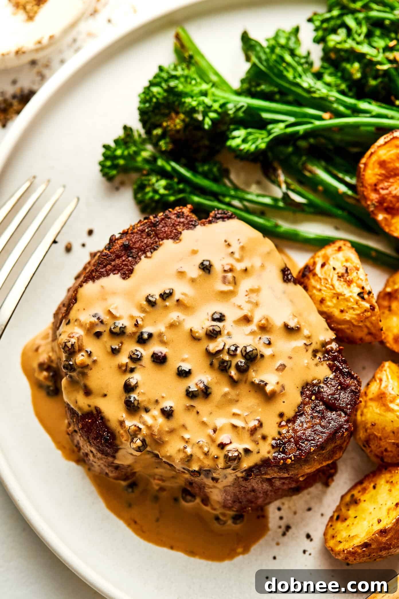 Filet Mignon with Peppercorn Sauce served on a plate with broccolini and roasted potatoes.