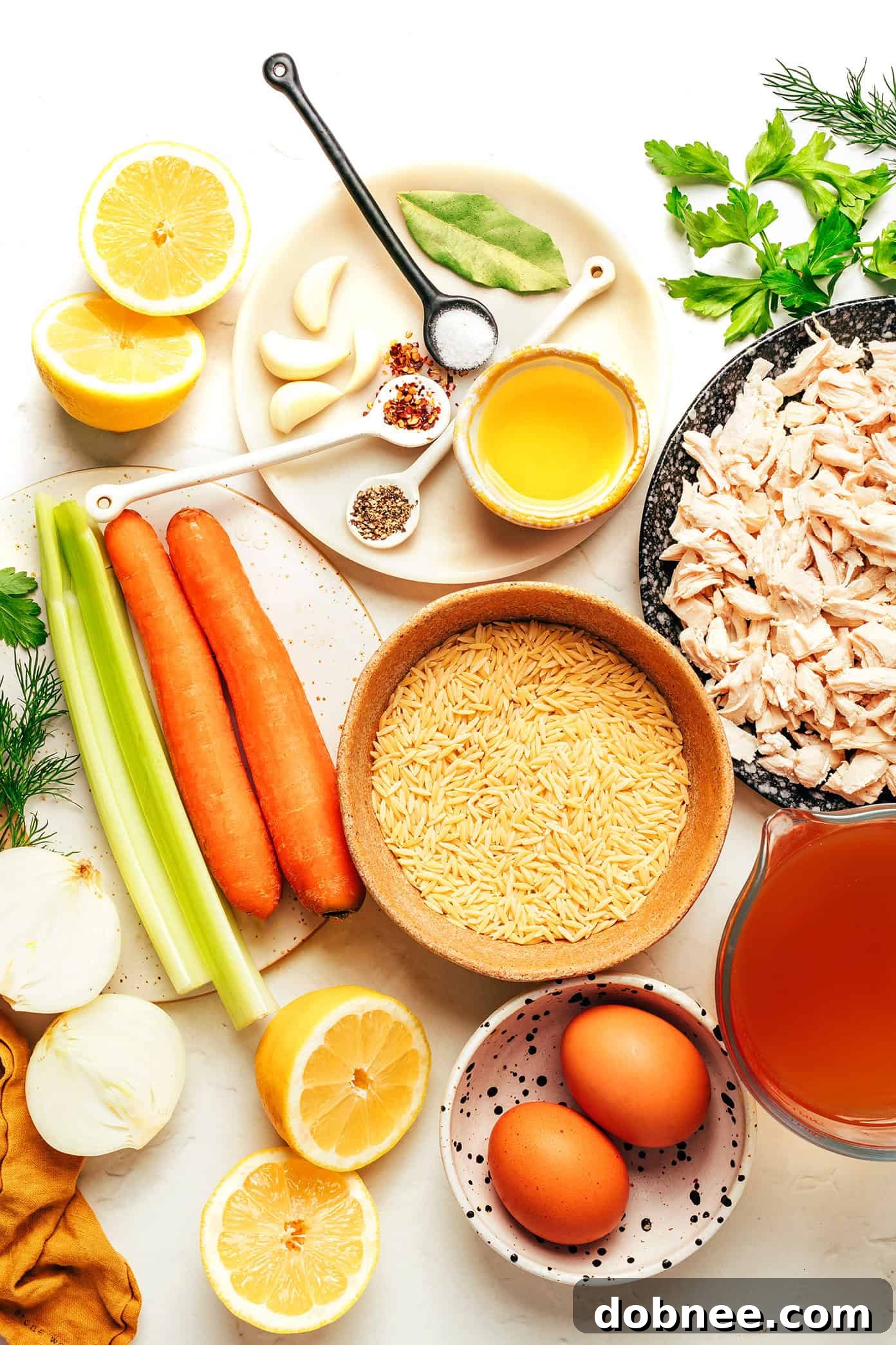 A rustic overhead shot of Lemony Orzo Chicken Soup in a bowl, showcasing the rich broth, tender chicken, and small pasta, with fresh herbs scattered on top.