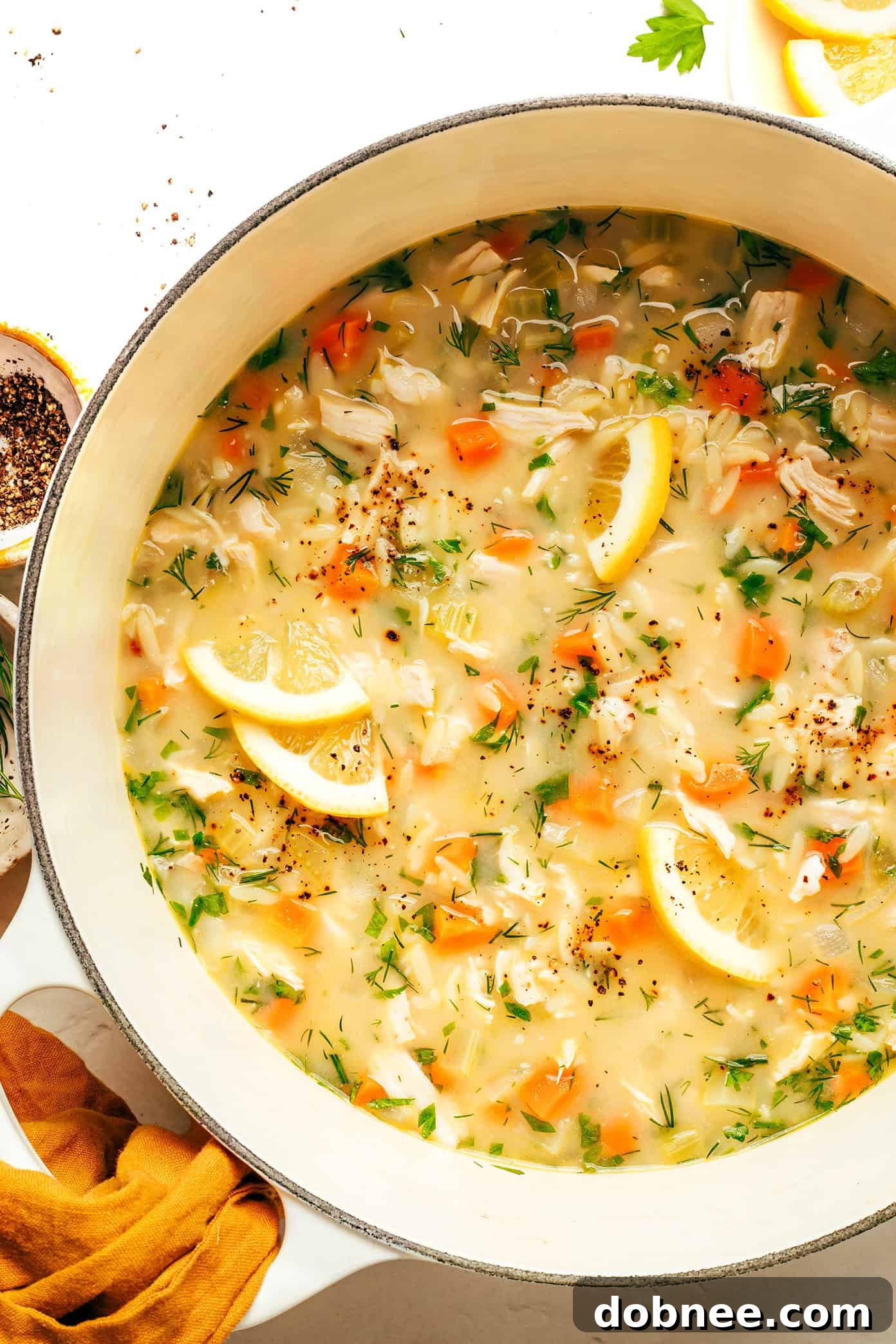 A vibrant close-up of a steaming bowl of Lemony Orzo Chicken Soup, garnished with fresh herbs and a lemon slice.