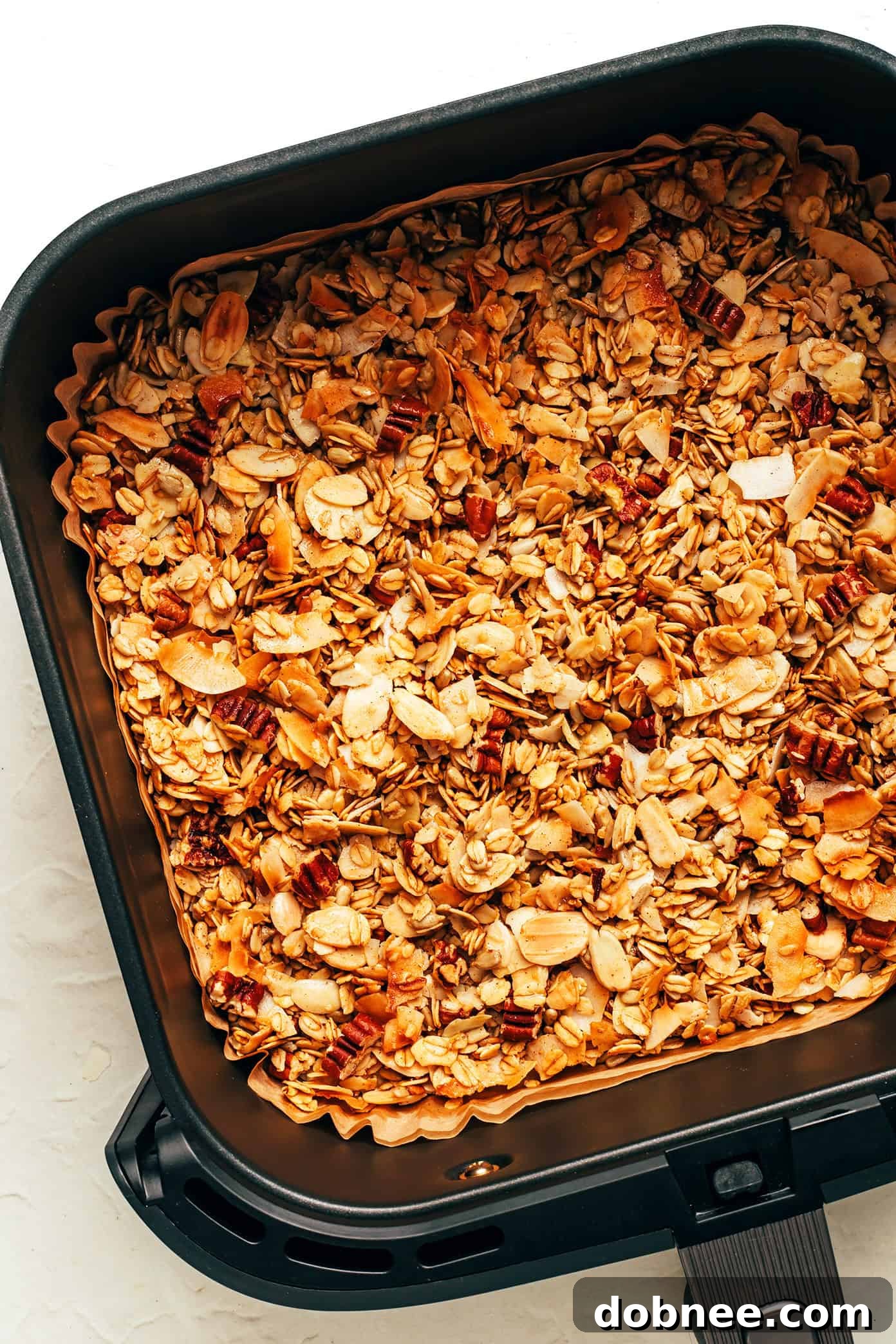 Close-up of golden brown air fryer granola in a bowl, showing crunchy oats, nuts, and coconut flakes.