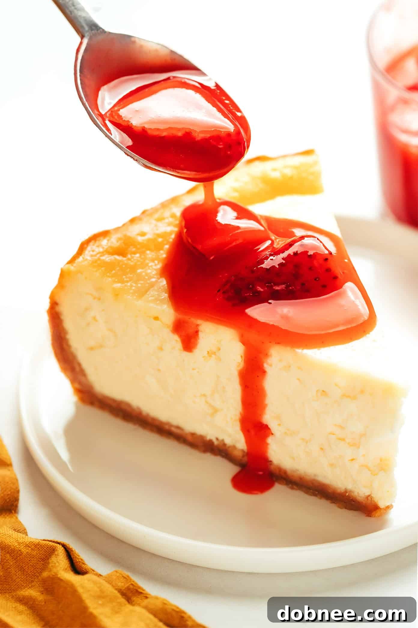 Strawberry sauce drizzled generously over a slice of cheesecake.