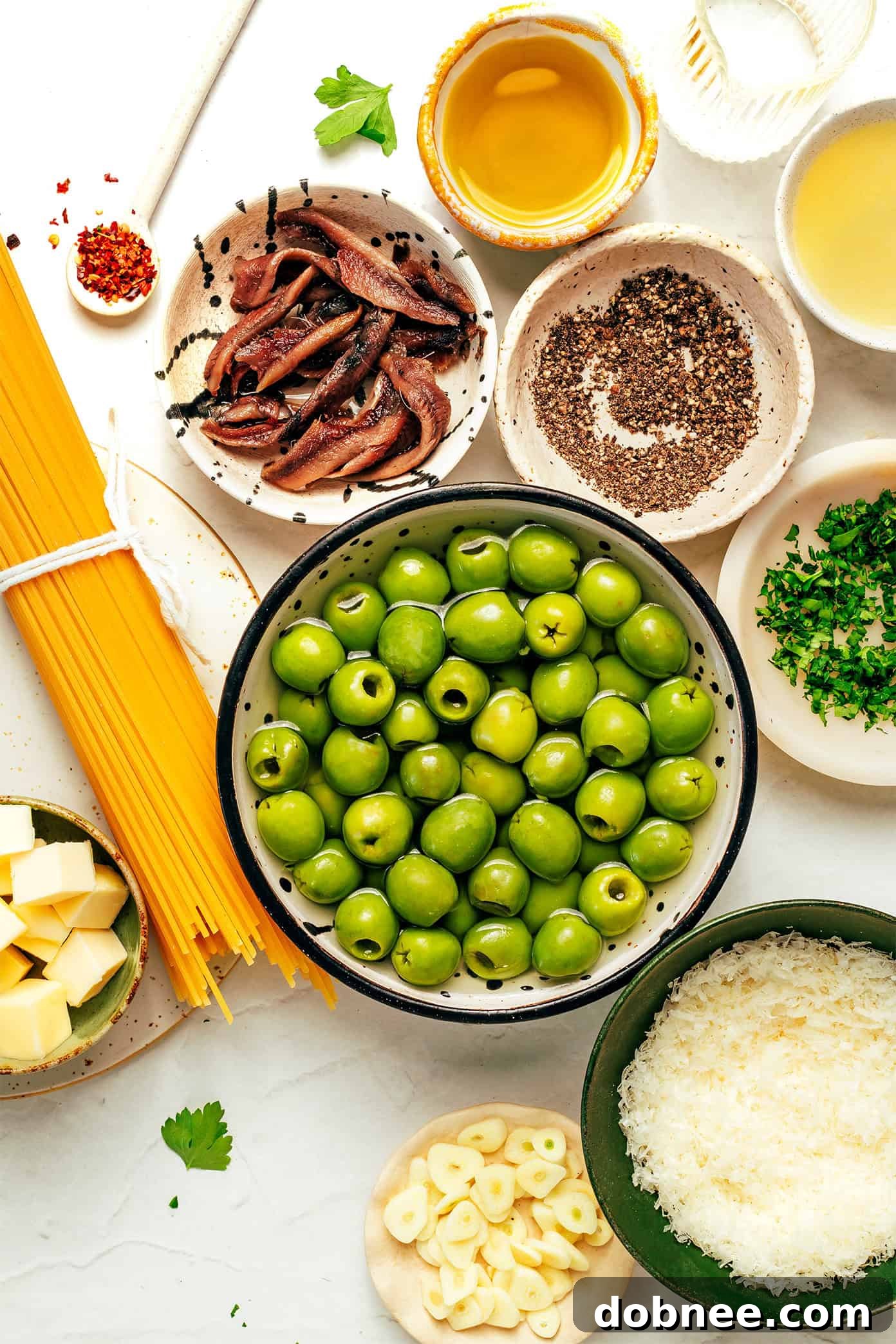 Ingredients for Dirty Martini Pasta laid out on a surface, including olives, garlic, and pasta.