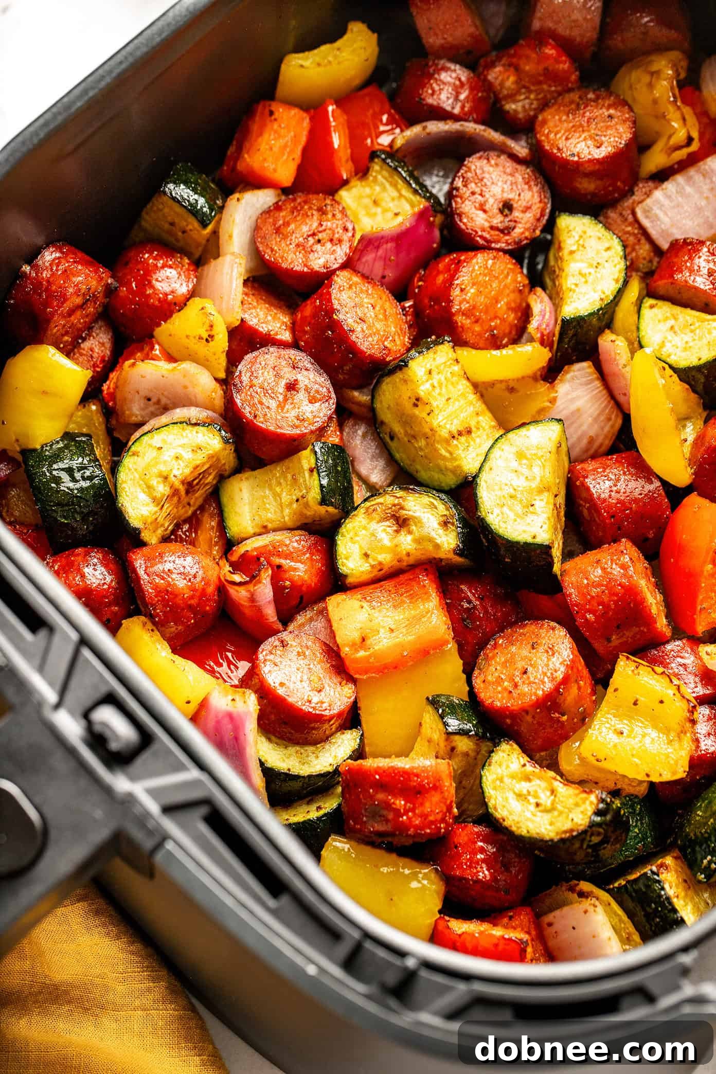 Air fryer sausage and vegetables being scooped from a serving bowl onto a plate.